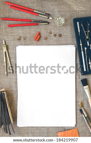 Blank paper sheet on canvas background with color pencils, crayons, chalks, brushes and drawing tools with retro filter effect