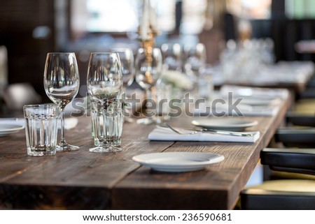 Glasses, forks, knives, napkins and decorative flower on a dark old brown wooden table served for dinner in cozy restaurant