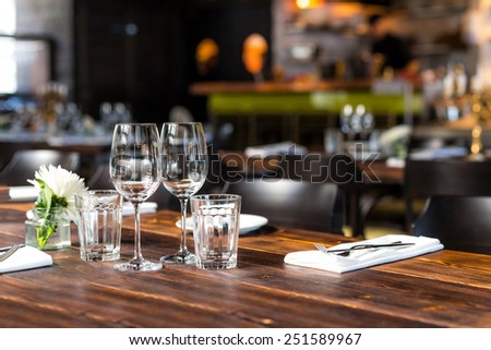 Glasses, flowers, forks, knives served for dinner in restaurant with cozy interior.