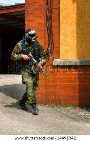Soldier with Rifle and Face Mask By Brick Wall