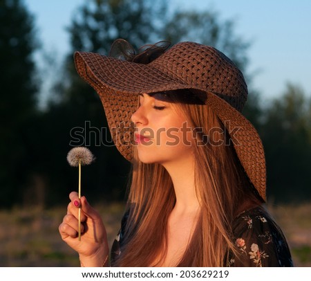 Young girl in wicker hat with dandelion in hand