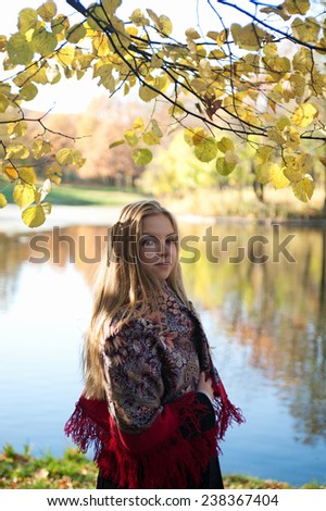 Girl with her blond hair on background of pond and yellow autumn trees