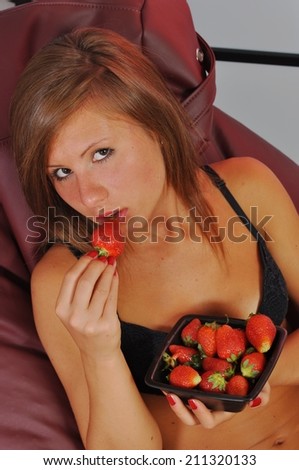 Portrait of woman eating strawberries. Healthy sensual and young smiling woman eating strawberry inside in bed holding a bowl of strawberries.