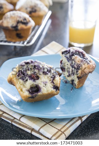 Open Blueberry Muffin on plate. With orange juice and other blueberry muffin in back.