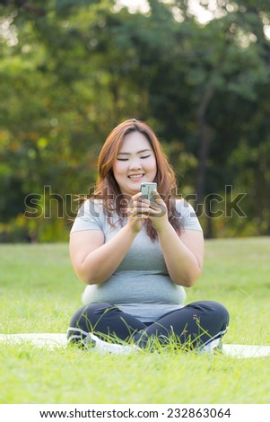 Beautiful obese woman playing mobile phone on the grass.