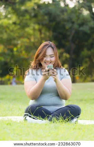Beautiful obese woman playing mobile phone on the grass.
