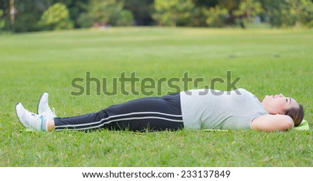 Obese woman do sit ups on grass.