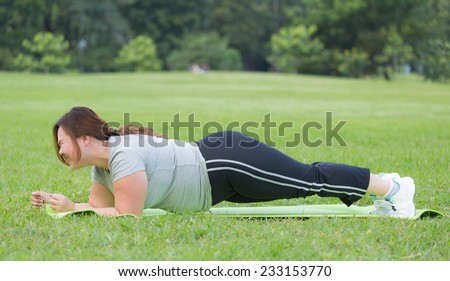 Obese woman doing plank on the grass.