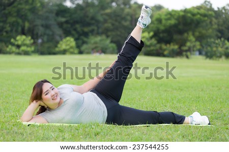 Obese woman side scissor kick exercise on the grass.