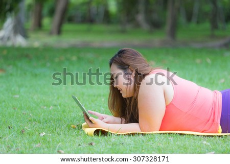 Beautiful fat woman using a tablet computer to relax in the park.