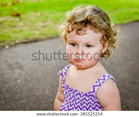Grumpy hot ,sweaty little girl at the park on a hot day, dropping her bottom lip.