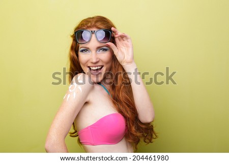 Funny woman applying sunscreen or suntan lotion on her shoulder. Skin care and protection concept with cream drawing of sun icon.