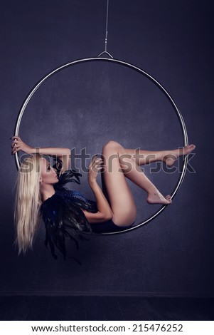 gymnast on a ring in circus under a dome. Young woman gymnast on rope on black background. Lovely tightrope walker in a trendy costume on a hoop in the circus. The concept of confidence and balance