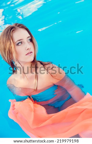 The girl with coral fabric sits in pool. beauty shot.
