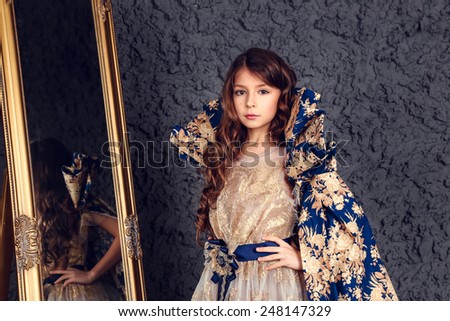 Little girl dressed as a princess in the mirror on the dark wall background, studio