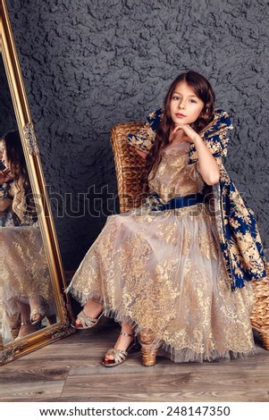 Little girl dressed as a princess in the mirror on the dark wall background, studio