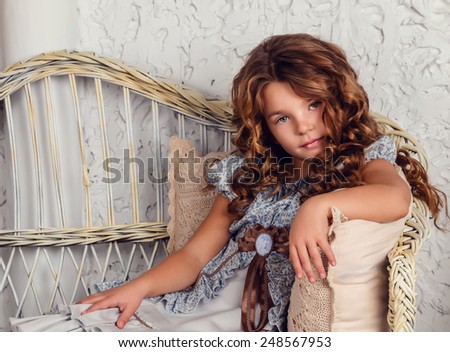 girl wearing stylish retro dress posing over white background. Wicker sofa and an easel with brushes