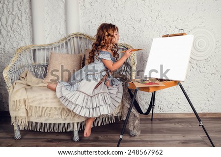 girl wearing stylish retro dress posing over white background. Wicker sofa and an easel with brushes