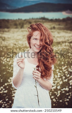Image of pretty woman lying down on chamomile field, happy female holding in hand beautiful white flower, cheerful girl resting on daisy meadow, relaxation outdoor in springtime, vacation concept