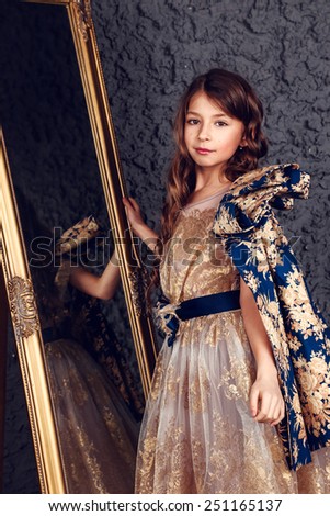 Little girl dressed as a princess on the dark wall background, studio