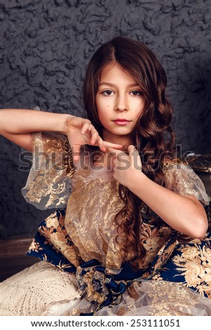 Little girl dressed as a princess on the dark wall background, studio