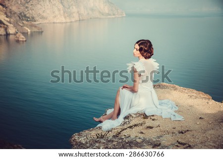 Beautiful bride posing on the coast with angelic dress. Bride in wedding dress stands on a cliff with a beautiful sea view from the top
