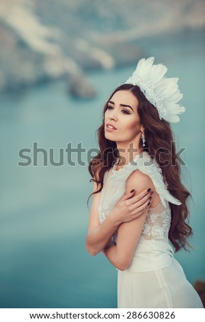 Beautiful bride posing on the coast with angelic dress. Bride in wedding dress stands on a cliff with a beautiful sea view from the top
