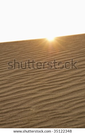 sun peaking over ridge of sand dune in Death Valley National Park, CA