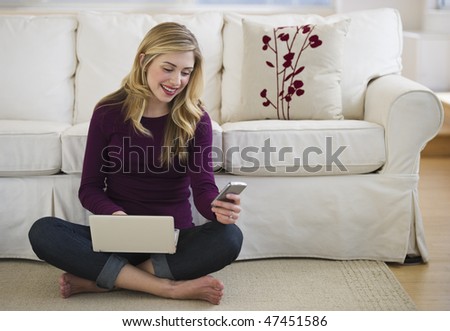 cheerful female on living room floor with laptop and cell phone