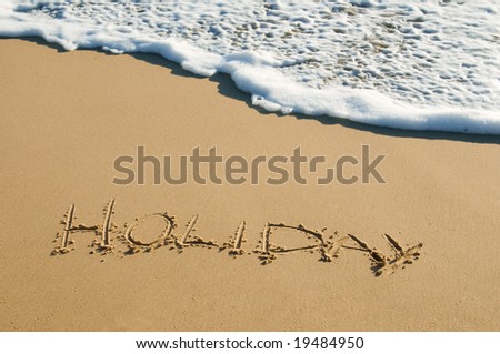 the word \'holiday\' written onto sand surface about to be washed away