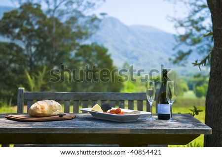 Alfresco with mountains in the background. Setting with wine, cheese, bread, tomatoes and advocado.