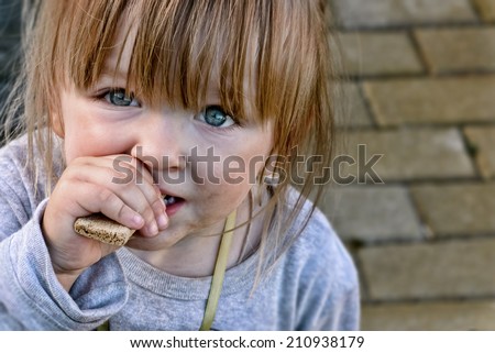 Hungry caucasian child with big clear eyes eating bread and impressively looking at the camera. Close-Up.