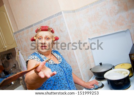 woman with curlers and cosmetic mask, preparing food on the kitchen