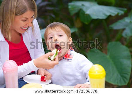 pretty young mother gives the child to bite piece of sandwich in the park