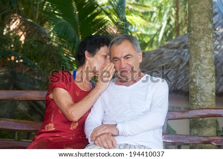 elderly couple on vacation: woman whispers something in the ear of the man