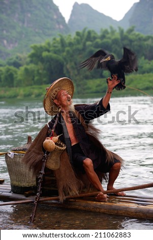 Elderly Chinese fisherman in traditional clothes of the ancient style of fishing using cormorants on the Lijiang River, Guangxi Province, China