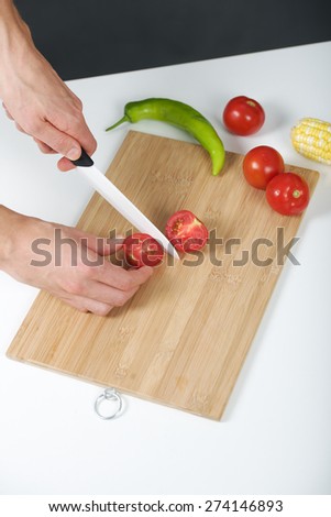 The left-hander Cook cuts tomato using ceramic knife on a board. Vertical photo