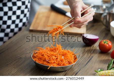 Chef makes spicy Korean carrot salad in a bowl. Vertical photo