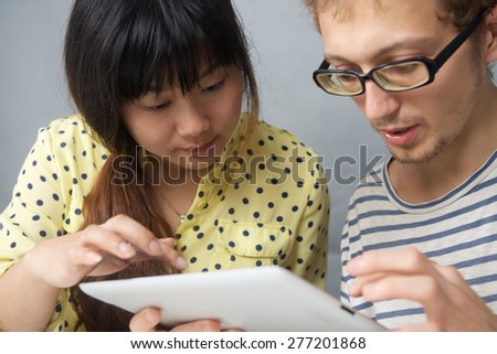 Caucasian young man together with a Chinese girl looking on tablet