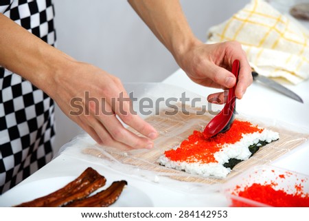 Cook put caviar prepares California roll sushi in the kitchen