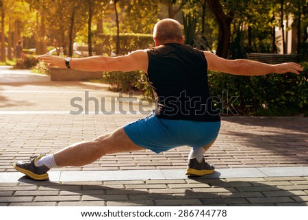 Happy elderly man doing exercises on urban district sports ground