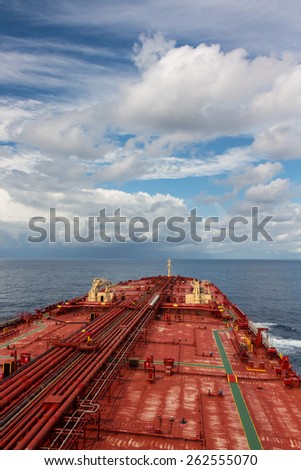 Deck of oil carrier ship under blue cloudy sky.