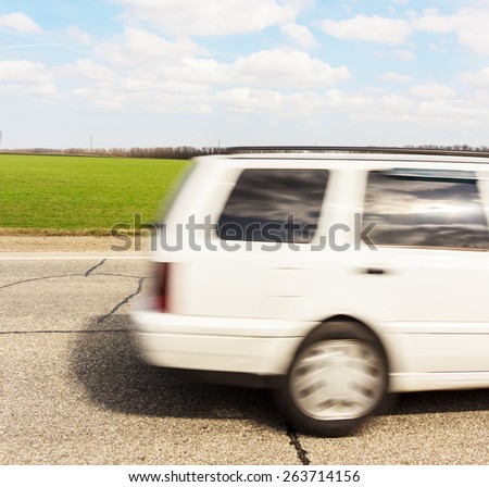 White moving car on an asphalt road on green field and blue sky background.