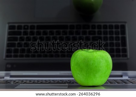 Green apple on a laptop with reflected keyboard on a screen.