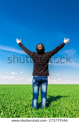 Man dressed in black shirt and blue jeans among blue sky and green field