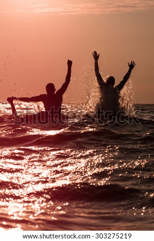 Couple of young men jumping with splashes in the sea.