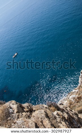 Top view of a deep blue sea and rocks of the coast. A little boat sailing
