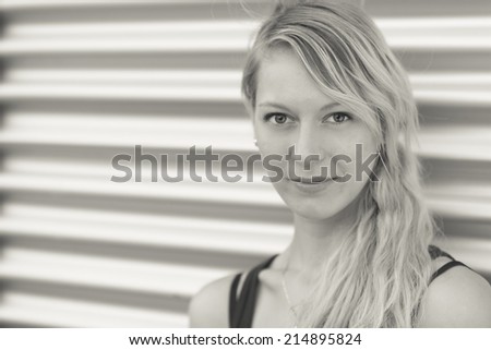 Young woman, with blonde hair leaning against a stainless steel garage door, image in black and white.