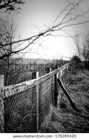 Black and white photograph showing a propped-up fence in the landscape leading off into the distance