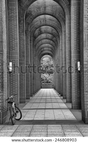 Bike Leaning on the front part of an arch corridor. A black and white image of a bike leaning on arch corridor. There are two white street lamps fixed on the arches.